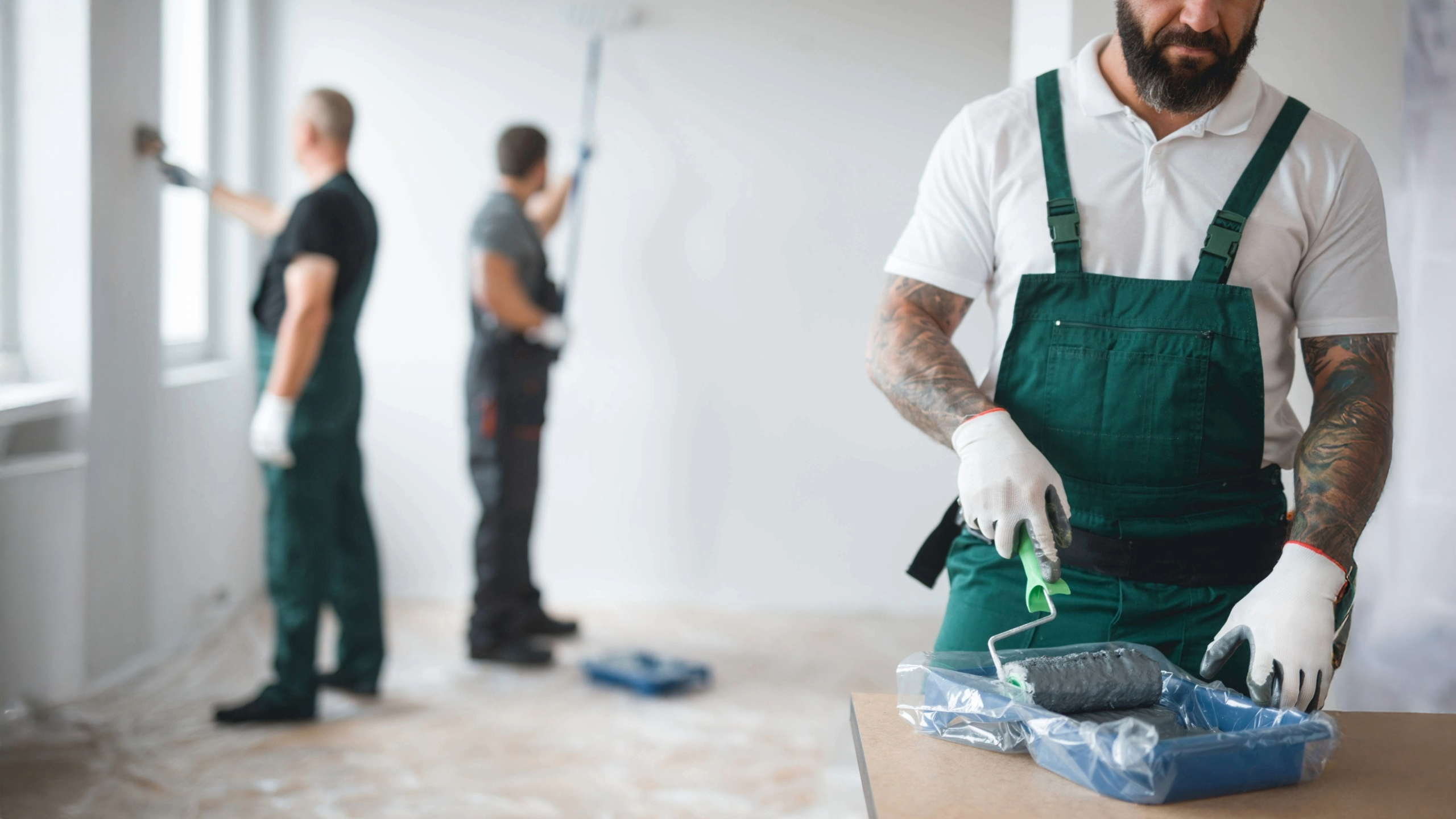 Team of professional painting contractors in work overalls preparing for an interior residential painting job using rollers and trays
